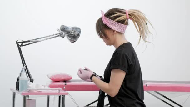 Retrato de um atraente mestre de tatuagem feminino. Menina elegante com dreadlocks em um fundo de estúdio branco e rosa . — Vídeo de Stock
