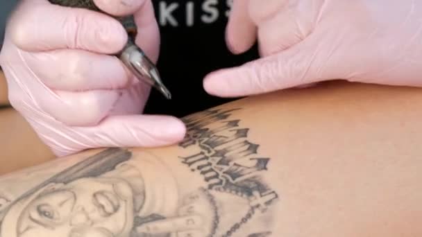 Tetoválás mester vonzó nő raszta tetoválások ügyfél a lány a csípő. Fekete tetoválás gép és tinta. Kép egy dühös apáca. Rózsaszín és fehér stúdió falháttér.