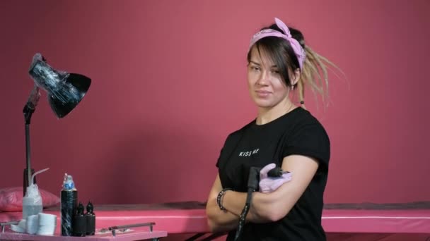 Porträtt av en attraktiv kvinnlig tatuering mästare. Snygg tjej med dreadlocks på en rosa bakgrund. — Stockvideo