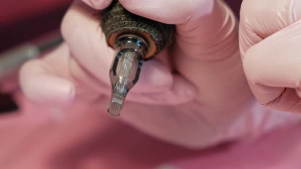 Le maître du tatouage insère une aiguille dans la machine à tatouer. Gants de sécurité roses sur fond rouge . — Video