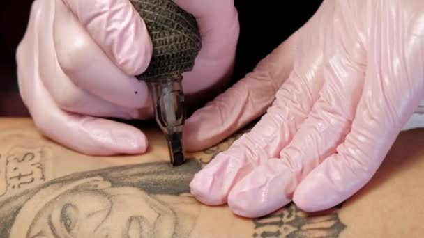 Tattoo Master aantrekkelijke vrouw met dreadlocks tatoeages cliënt aan het meisje op de heup. Zwarte tattoo machine en inkt. Foto van een boze non. Roze en witte Studio muur achtergrond. — Stockvideo