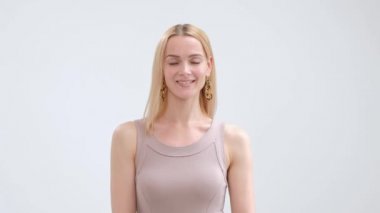 Bej elbise çekici zarif sarışın kadın poz ve beyaz bir arka planda gülümseyen.