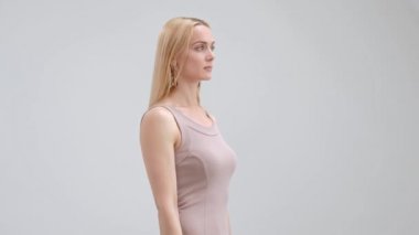 Bej elbise çekici zarif sarışın kadın poz ve beyaz bir arka planda gülümseyen.