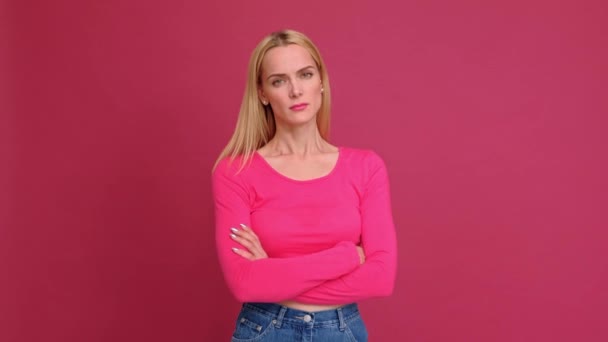 Mulher jovem loira atraente em uma camiseta vermelha e jeans posando em um fundo rosa. Mostra emoções diferentes, surpresa, alegria, tristeza . — Vídeo de Stock