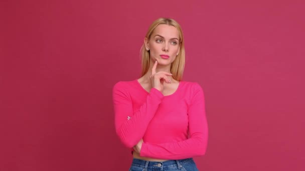 Приваблива молода жінка блондинка в червоній футболці і джинсах позує на рожевому тлі. Показує різні емоції, сюрприз, радість, смуток . — стокове відео