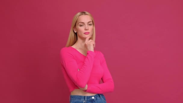 Atractiva joven rubia con una camiseta roja y jeans posando sobre un fondo rosa. Muestra diferentes emociones, sorpresa, alegría, tristeza . — Vídeos de Stock