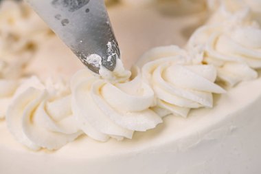 Decorating a white cake with cream from the pastry bag. Macro shot, closeup. clipart