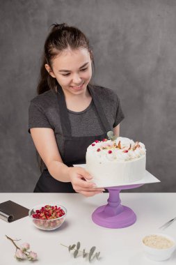 Çekici genç kadın esmer şekerci bir gıda gül küçük kırmızı çiçekler ile beyaz bir kek sunar.