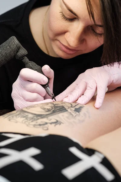 Kadın dövme ustası kadın müşteri dövme. Uyluk üzerindeki rahibeler. Siyah dövme makinesi ve lamba. İşyeri sanatçısı. — Stok fotoğraf