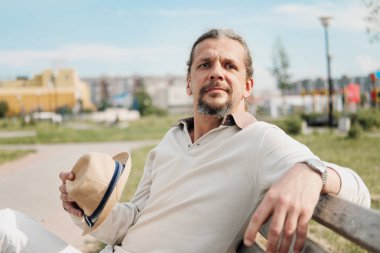 Kuyruk uzun saçlı bir çekici yaşlı 50-yaşındaki adam bir bankta bir umumi bahçede oturur. Sıcak yaz günü, açık bej giyim.