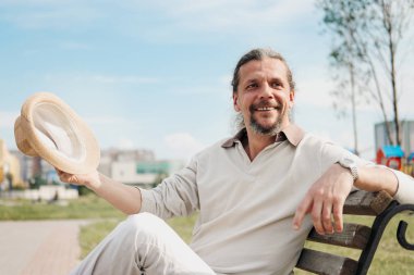 Kuyruk uzun saçlı bir çekici yaşlı 50-yaşındaki adam bir bankta bir umumi bahçede oturur. Sıcak yaz günü, açık bej giyim.