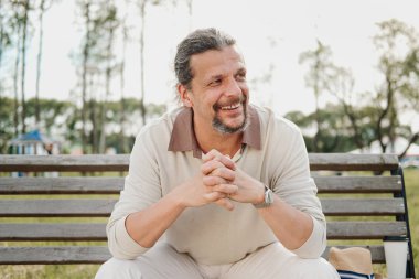 Kuyruk uzun saçlı bir çekici yaşlı 50-yaşındaki adam bir bankta bir umumi bahçede oturur. Sıcak yaz günü, açık bej giyim.