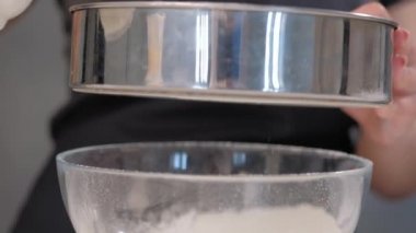 Cook kadın gri bir arka planda bir elek ile unu elemek.