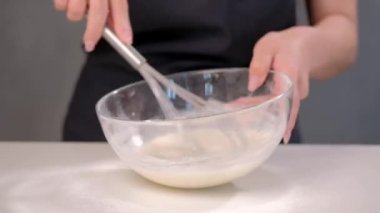 Bir kadın aşçı pasta şefi bir metal fırçalama ile bir cam kase hamur kamçılamak.