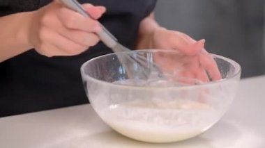 Bir kadın aşçı pasta şefi bir metal fırçalama ile bir cam kase hamur kamçılamak.