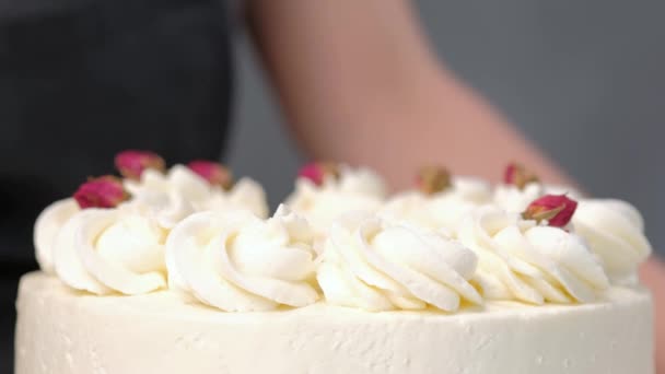 Vonzó fiatal női barna cukrászda díszíti a fehér torta, kis piros virágokkal az élelmiszer-Rózsa csipesszel. — Stock videók