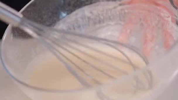 女性の料理人のペストリーシェフは、金属の泡立て器でガラスボウルに生地をホイップ. — ストック動画