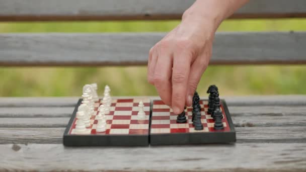Playing chess outdoor. Chess board and figures on the bench, against the backdrop of greenery. Close-up. — Stock Video