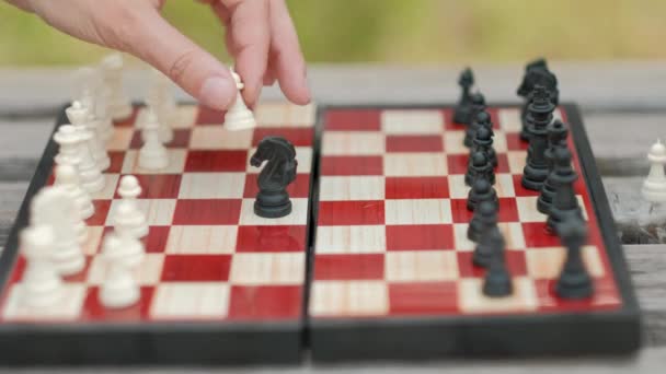 Schach spielen im Freien. Schachbrett und Figuren auf der Bank, vor der grünen Kulisse. Nahaufnahme. — Stockvideo