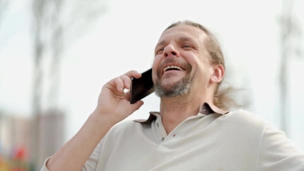 Klidný atraktivní muž středního věku s dlouhými šedými vlasy hovoří na telefonu, směje se a usměje se. — Stock video