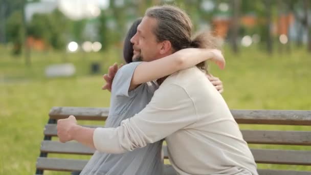 Een ontspannen aantrekkelijke man van middelbare leeftijd met lang grijs haar en een jonge vrouw met geverfd haar knuffelen en groet. — Stockvideo