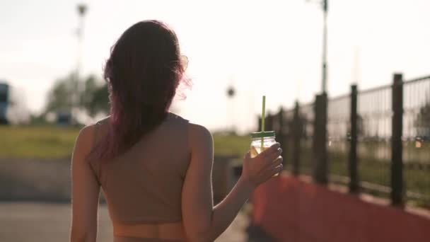 Jeune belle femme en lunettes de soleil boit un cocktail dans un bocal en verre avec une paille dans une rue de la ville . — Video