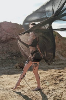 Siyah iç çamaşırı güzel seksi kadın. Vücut birçok dövmeler ile kaplıdır. Kafasından dreadlocks. Kumlu kariyer ve siyah kumaş karşı poz.