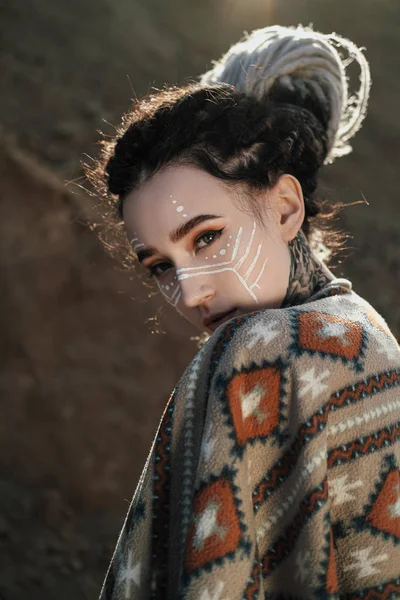Mulher bonita com orelhas de elfo, dreadlocks e um poncho étnico, com rosto pintado. Posando contra uma carreira arenosa ou deserto . — Fotografia de Stock