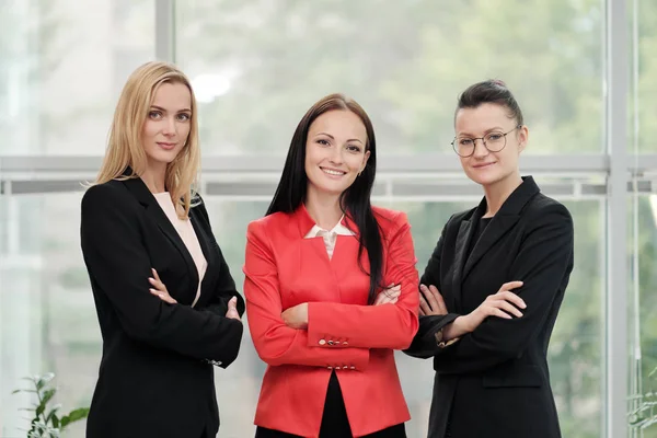 İş elbiseli üç genç çekici kadın bir ışık ofisi arka planda poz. Baş ve astlar. Profesyonel ve iş arkadaşları çalışma ekibi. — Stok fotoğraf