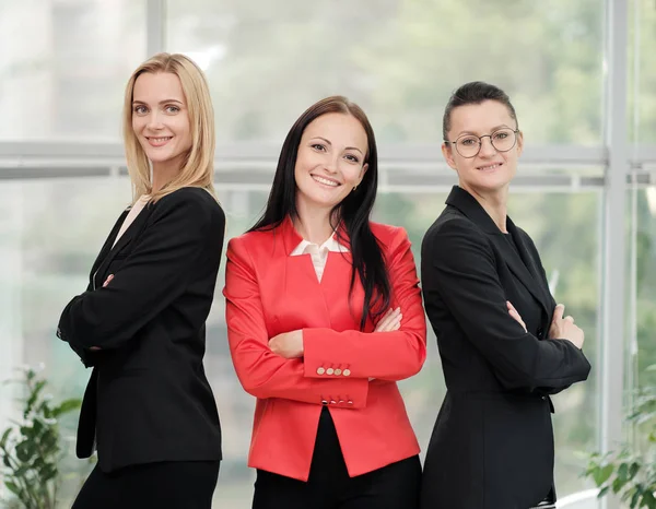 Drie jonge aantrekkelijke vrouwen in business suits poseren tegen de achtergrond van een licht kantoor. Hoofd en ondergeschivelde. Werk team van professionals en collega's. — Stockfoto