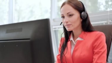 Kırmızı ceket içinde yönetici başında masanın üzerinde oturan Red Jacket genç çekici kadın. Mikrofon ile kulaklıklar video konferansı tutar. Beyaz bardak kahve içme.