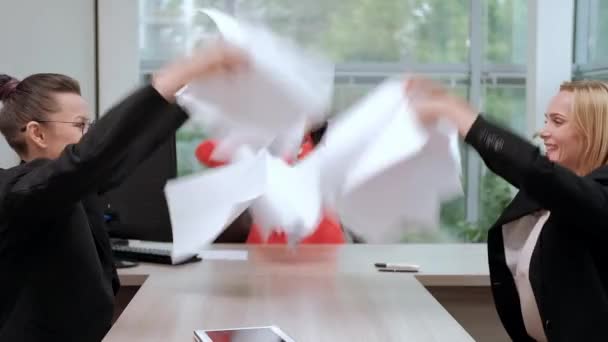 Tres hermosas chicas jóvenes en trajes de negocios están sentadas en el escritorio de la oficina. Cansado del trabajo. Tira aviones de papel y ríete. Descanso y descanso . — Vídeo de stock