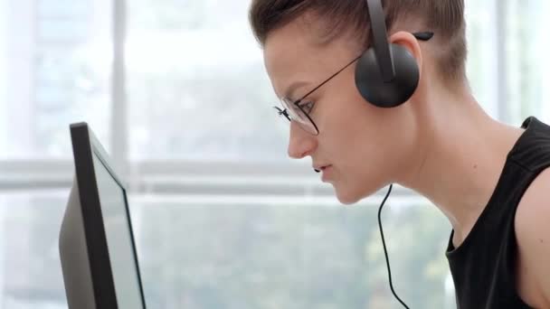 Een jonge aantrekkelijke vrouw die een zwarte jas in een zwarte jas draagt zit aan haar Bureau in een Executive Chair. Houdt een videoconferentie in een koptelefoon met een microfoon. — Stockvideo