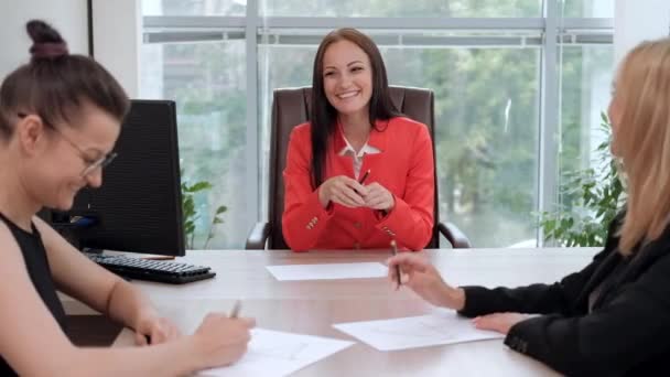 Três jovens mulheres atraentes em trajes de negócios estão sentadas em uma mesa e discutindo fluxos de trabalho. Cabeça e subordinados. Equipe de trabalho de profissionais e colegas . — Vídeo de Stock