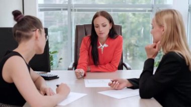 İş elbiseler üç genç çekici kadın bir masada oturuyor ve iş akışları tartışıyor. Baş ve astlar. Profesyonel ve iş arkadaşları çalışma ekibi.