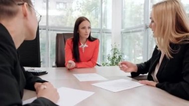 İş elbiseler üç genç çekici kadın bir masada oturuyor ve iş akışları tartışıyor. Baş ve astlar. Profesyonel ve iş arkadaşları çalışma ekibi.