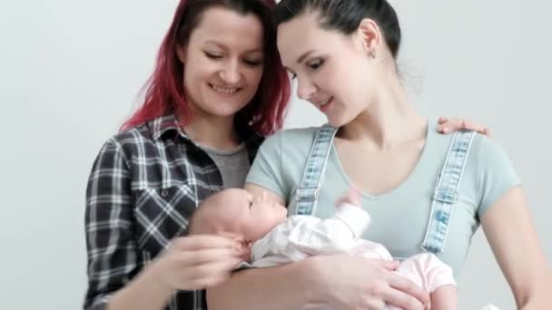 Две молодые женщины с ребенком на белом фоне. Однополые браки и усыновление, гомосексуальная лесбийская пара . — стоковое видео