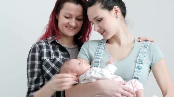 Zwei junge Frauen mit einem Baby auf weißem Hintergrund. gleichgeschlechtliche Ehe und Adoption, homosexuelles lesbisches Paar. — Stockvideo