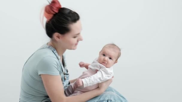 Denim tulum genç kadın anne kucağında bir bebek çocuk tutar. Stüdyoda beyaz arka plan. — Stok video