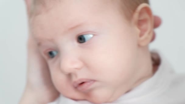 Young woman mother in denim overalls holds a baby child in her arms. White background in the studio. — Stock Video