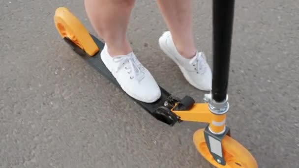 Attraktiv ung kvinna med färgat hår i en Jeansklänning och vita sneakers som rider på en spark skoter genom gatorna i staden. — Stockvideo