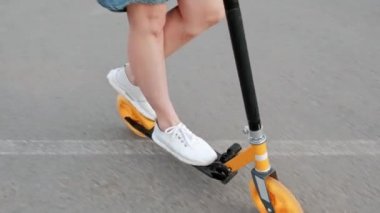 Bir Denim elbise ve şehir sokaklarında bir Kick Scooter sürme beyaz spor ayakkabıları boyalı saçlı çekici genç kadın.