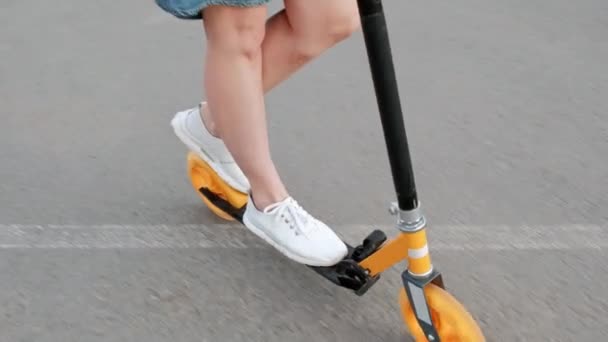 Приваблива молода жінка з фарбованим волоссям у джинсовій сукні та білими кросівками, що їздять на скутері по вулицях міста . — стокове відео