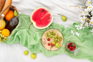 Yeşil çim üzerinde çayırda yaz pikniği. Meyve sepeti, meyve suyu ve şişe şarap, karpuz, çilek bir cam kavanoz ve ekmek Bagetler. Beyaz masa örtüsü ve bir buket alan papatyalar.