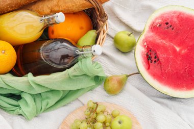 Yeşil çim üzerinde çayırda yaz pikniği. Meyve sepeti, meyve suyu ve şişe şarabı, karpuz ve ekmek bagetleri. Beyaz masa örtüsü ve bir buket alan papatyalar.