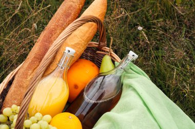 Yeşil çim üzerinde çayırda yaz pikniği. Meyve sepeti, meyve suyu ve şişe şarap, karpuz, çilek bir cam kavanoz ve ekmek Bagetler. Beyaz masa örtüsü ve bir buket alan papatyalar.