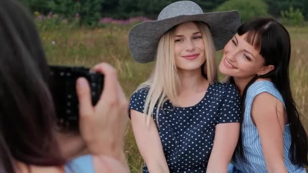 Trois jeunes jolies filles sur un pique-nique. Le photographe prend des photos sur l'appareil photo sans miroir de deux modèles. Les modèles posent et regardent des photos . — Video