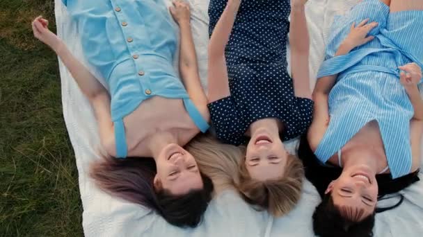 Drei junge attraktive Frauen liegen auf einem Karo und blicken in den Himmel. Lachen und nach oben zeigen, tanzen. Ruhe Freundinnen im Freien Natur. — Stockvideo