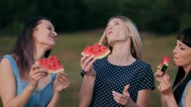 Gün batımı mavi elbiseler üç genç çekici kadın arkadaşlar karpuz yiyor ve gülümseyen.