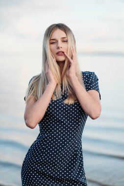 Genç çekici sarışın kadının portresi, mavi bir elbise açık havada, yüzünde eller.